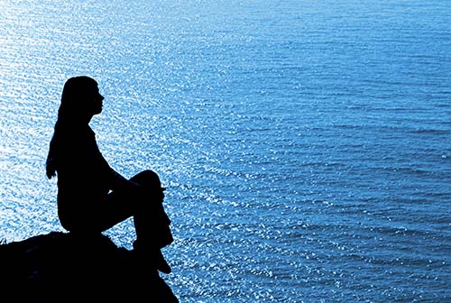 Una dama sentada sobre un peñasco alto, en silueta, con el mar de frente, ilustra el tema De gran manera impactante un escrito sobre los Malos Pensamientos, en editoriallapaz. 