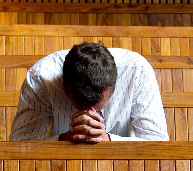 This focus on a man bowed in prayer in a church building setting illustrates the paragraph on prayer in the article We Invite You to Learn About the Church Christ Built, in iglesia-de-cristo.com.