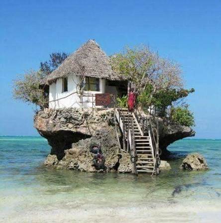 Fotografía de una casa edificada sobre una piedra alta y ancha en aguas playeras del mar, ilustración para Beneficios de huracanes.