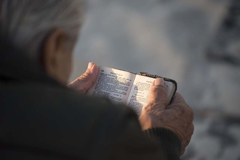 Un anciano sostiene la Biblia en sus manos, leyéndola, fotografía que ilustra la Declaración sobre quien es cómo funciona un evangelista según el Nuevo Testamento de Cristo.