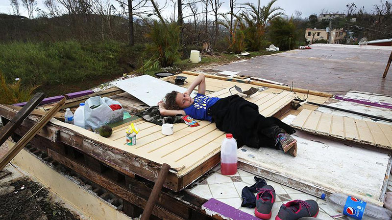 En Coamo, Puerto Rico, por el lado sur de la isla, una niña joven descansa sobre un canto de piso de la casa donde vivía antes de que el huracán María destruyera las paredes y el techo de la estructura, también arrasando con los muebles, etcétera.