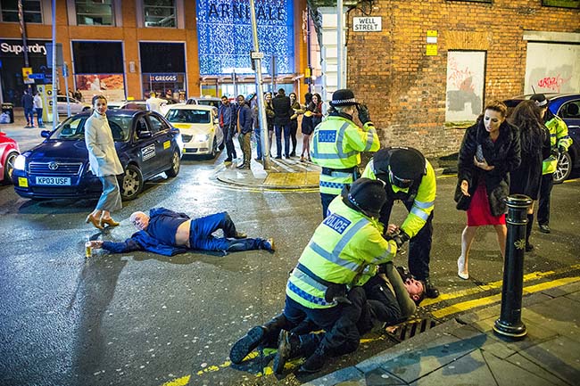 La famosísima fotografía “La creación de Manchester.” La policía detiene a un hombre violento parrandero de Víspera de Año Nuevo, mientras otro parrandero bien borracho yace en la calle con su brazo derecho extendido hacia una botella de cerveza.