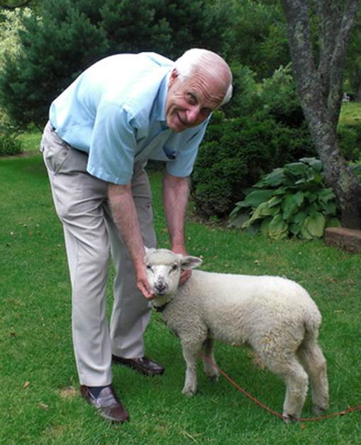 Foto de un varón anciano que, inclinándose, toma en sus manos la cabeza de una oveja.
