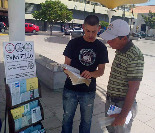 En esta fotografía un adulto joven reparte folletos e imparte enseñanzas bíblicas en un área comercial.
