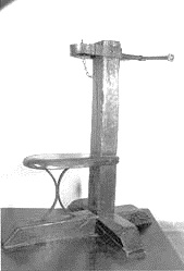 Estructura de madera con un asiento curvado y un poste vertical provisto de un collar de hierro en la parte superior.