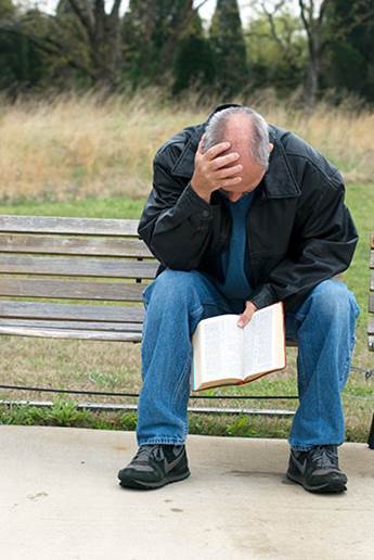 Un varón sesentón, sentado en un banco, cabecibajo, como muy triste y perdido, lee la Biblia, foto para el tema: Realmente, ¡la mejor fuente de psicología efectiva, terapia y alivio para el alma, espíritu y corazón.