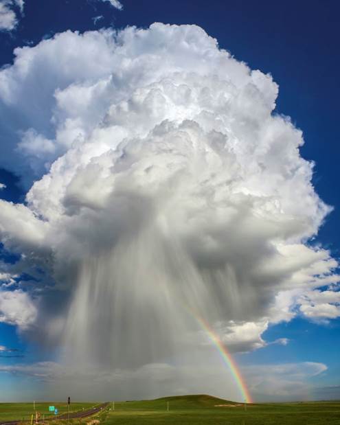 Photograph of a tall, isolated cumulus cloud with part of a rainbow on one side.