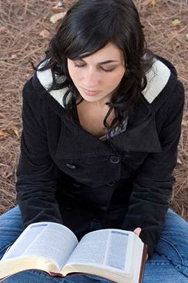 Fotografía de una dama joven que sentada lee su Biblia.