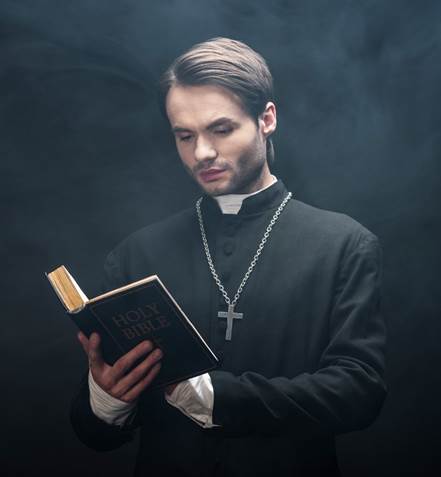 Fotografía de un sacerdote católico romano que sostiene una Biblia abierta en las manos mientras la lee, contra un trasfondo negro.