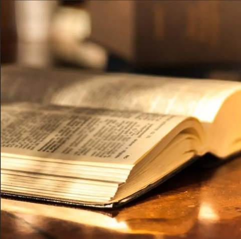  Fotografía de una Biblia abierta iluminada sobre una mesa de madera con el trasfondo difuminado, ilustraciones para estudios sobre la organización y las actividades de la iglesia primitiva del siglo I.