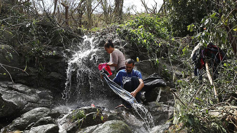 Cerca del pueblo de Aibonito, en las montañas altas del centro de Puerto Rico, una pareja lava ropa en las aguas cristalinas y frescas de una quebrada, mostrando la vegetación y los árboles alrededor de ellos los efectos de los vientos muy recios del huracán María.