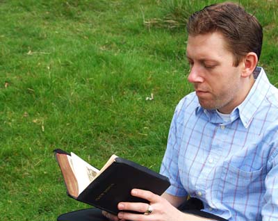 Esta fotografía de un varón sentado en un campo de hierba verde y leyendo su Biblia ilustra el artículo La iglesia ideal, según Dios, en editoriallapaz.