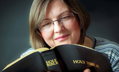 This photograph of a smiling woman reading the Bible illustrates the subject The Ideal Church, According to God, in editoriallapaz.org. 