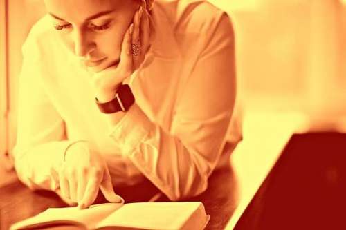 Fotografía de una mujer joven que lee la Biblia abierta, con trasfondos de tonos amarillos.