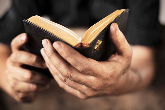 Photograph upclose of an open Bible in a man's hands for the study on the thrones of the apostles in Heaven.
