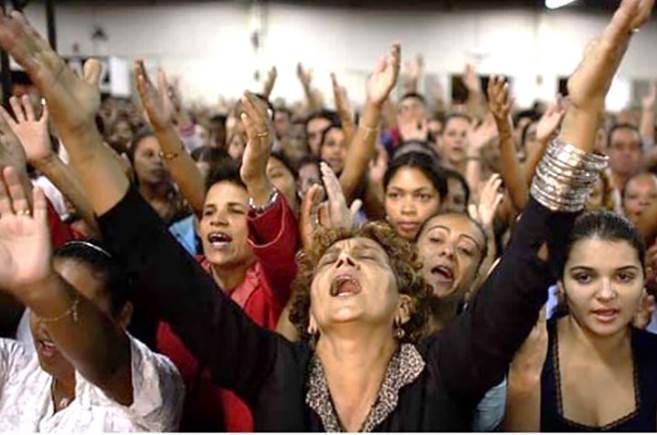 Esta fotografía de una congregación de pentecostales de pie, con los brazos levantadosy gritando todos a la vez a todo pulmón ilustra lo tanto Dios como el Sentido Común denuncian como culto NO aprobado por Cristo en su iglesia.