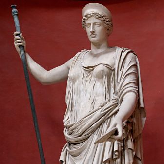 Estatua clásica de mármol de una mujer de pie con túnica drapeada, una tiara y sosteniendo una vara o cetro largo.